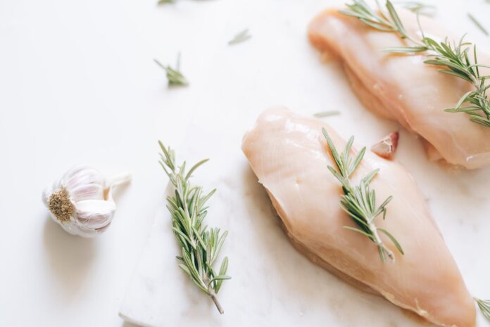 fresh raw chicken meat with rosemary toppings on white surface